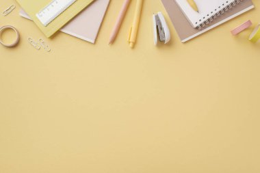 Okul konseptine geri dönelim. Okul malzemelerinin en üstteki fotoğrafı not defterleri cetvel kalemler, izole edilmiş pastel sarı arka planda mini zımba ve yapışkan bant klipsliyor.