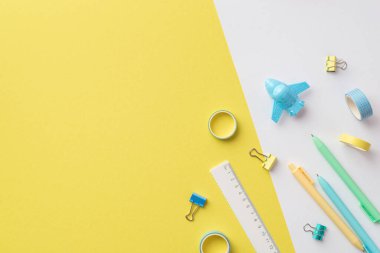 Back to school concept. Top view photo of school accessories plane shaped sharpener pens ruler adhesive tape and binder clips on bicolor yellow and white background with copyspace