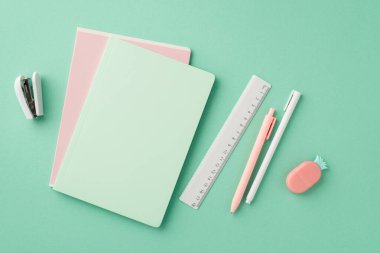 Okul konseptine geri dönelim. Kırtasiye fotokopi kitaplarının üst görünümü kalem cetvel zımba ve ananas şekilli silgi izole edilmiş pastel yeşil arka plan