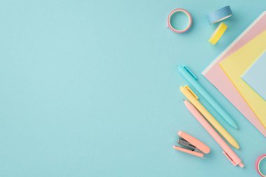 School accessories concept. Top view photo of school supplies mini stapler adhesive tape colorful pens and copybooks on isolated pastel blue background with copyspace