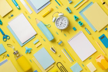 Alarmlı saat günlüklerinin, kalem kılıfının, raptiyelerin, raptiyelerin, hesap makinelerinin, cetvellerin, alfabe harflerinin, izole edilmiş sarı arkaplandaki bant keskinleştirici şeklindeki uçak bantlarının en üstteki fotoğrafı.