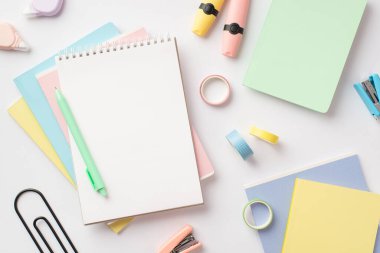 Okul konseptine geri dönelim. Not defterlerinin üst görünüm fotoğrafı kalem mini zımbaları yapışkan bant yuvarlak düzeltme bandı ve izole edilmiş beyaz arkaplan üzerindeki işaretleyiciler boş alan