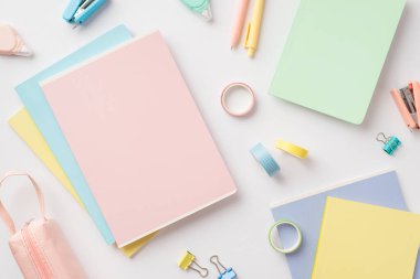 Okul konseptine geri dönelim. Not defterlerinin üst görünüm fotoğrafı kalem kutusu mini zımbaları yapışkan bant yuvarlak düzeltme bandı ve izole edilmiş beyaz arkaplan üzerindeki klasör klipleri