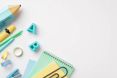 Okul konseptine geri dönelim. Okul malzemelerinin en üstteki fotoğrafı plastik alfabe harfleri mavi kalem kutusu not defterleri yapışkan bant mini zımba işaretleyicisi ve boş arkaplan üzerine kalemler.