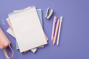 Back to school concept. Top view photo of stack of notepads pens stapler ruler clips and pink pencil-case on isolated violet background with blank space