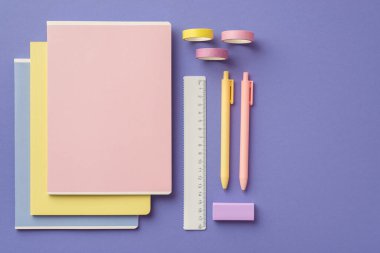 Okul konseptine geri dönelim. Renkli okul malzemelerinin en iyi görüntüsü. Defter yığını. Cetvel silgi ve izole edilmiş menekşe arkaplan bandı.