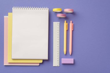 Okul konseptine geri dönelim. Renkli okul malzemelerinin en iyi görüntüsü. Bir yığın planlayıcı kalem silgi ve izole edilmiş mor arkaplan üzerine yapıştırıcı bant.