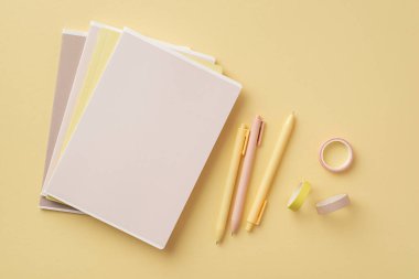 Okul aksesuarları konsepti. Kırtasiye defterlerinin üst görünüm fotoğrafı yapışkan bant ve izole edilmiş pastel arkaplan üzerindeki kalemler