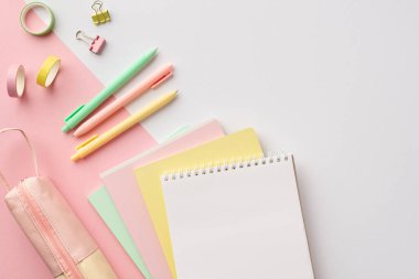Okul konseptine geri dönelim. Renkli okul malzemelerinin en üstteki fotoğrafı not defterleri, yapıştırıcı bant klipleri ve iki renkli beyaz ve pembe arka planda boş alan üzerine kalem kılıfı.