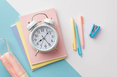 Okul konseptine geri dönelim. Okul malzemelerinin en üst görüntüsü alarm saatini not defterlerinin üzerine zımba telleri ve çift renkli mavi ve beyaz arka planda kalem kılıfı.