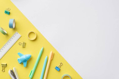 Okul konseptine geri dönelim. Dağınık kırtasiye uçağının üst görünüm fotoğrafı kalemleri şekillendirdi cetvel yapıştırıcı bant zımbası ve iki renkli sarı ve beyaz arkaplan üzerine bağlayıcı klipler boş alan