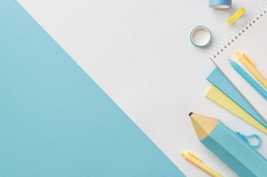 Okul konseptine geri dönelim. Sarı ve mavi kırtasiye notlarının en üst görünüm fotoğrafı çift renkli mavi ve beyaz arkaplan üzerine yapıştırıcı bant ve kalem kutusu.