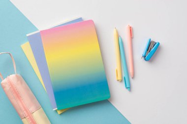 Back to school concept. Top view photo of school supplies gradient color copybook pens mini stapler and pink pencil-case on bicolor blue and white background