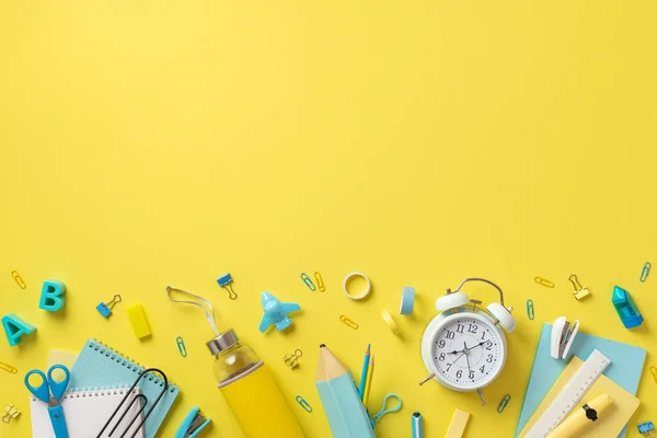 Top view photo of school supplies alarm clock notebooks bottle scissors alphabet letters clips stapler plane shaped sharpener pencil-case adhesive tape ruler isolated yellow background with copyspace