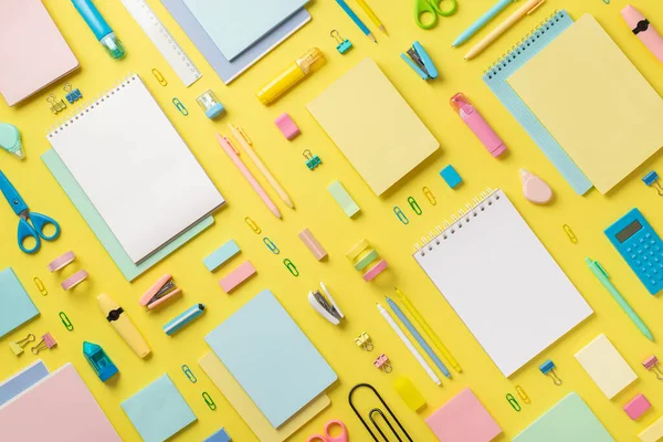 Back to school concept. Top view photo of copybooks correction pens binder clips stapler calculator ruler adhesive tape scissors sharpener eraser sticky note paper on isolated yellow background