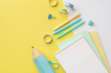 School accessories concept. Top view photo of blue pencil-case stack of copybooks colorful pens binder clips and adhesive tape on bicolor yellow and white background