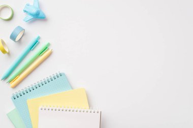 Okul aksesuarları konsepti. Renkli kırtasiye günlüklerinin üst görünümü düzlem şekillendirilmiş kalemler ve izole edilmiş beyaz arkaplan üzerine yapıştırıcı bant boş alan