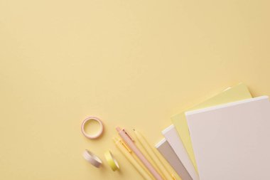 Okul konseptine geri dönelim. Okul malzemelerinin en üstteki fotoğrafı not defterleri yapıştırıcı bant ve boş alan ile izole edilmiş pastel sarı arka plan üzerindeki kalemler.