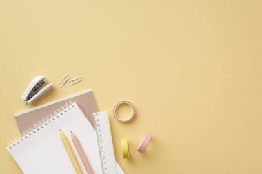Okul aksesuarları konsepti. Okul malzemelerinin en üst görüntüsü not defterleri cetvel kalemleri izole edilmiş pastel sarı arka planda mini zımba ve yapışkan bant klipsliyor