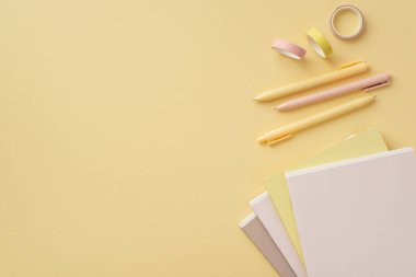 Okul konseptine geri dönelim. Ofis malzemelerinin üst görüntüsü not defterleri yapıştırıcı bant ve kalemler izole edilmiş pastel sarısı arka planda, kopyalanmış