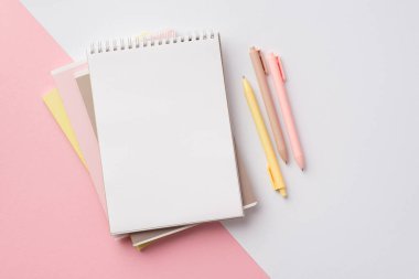 Back to school concept. Top view photo of school supplies stack of notebooks and pens on bicolor pink and white background
