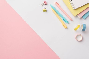 Back to school concept. Top view photo of stationery stack of colorful notepads pens binder clips and adhesive tape on bicolor white and pink background with copyspace