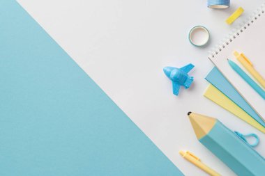 Okul malzemeleri konsepti. Sarı ve mavi okul aksesuarlarının, uçak şeklindeki kalemlerin, kalemlerin, yapıştırıcı bantların ve çift renkli mavi ve beyaz arka planların en üst görüntüsü.
