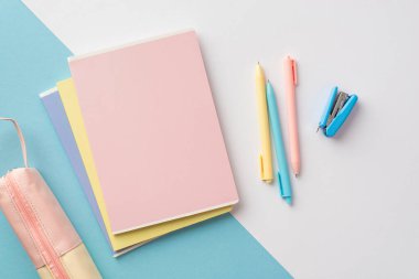 Back to school concept. Top view photo of colorful school supplies stack of copybooks pens mini stapler and pink pencil-case on bicolor blue and white background