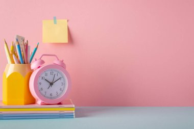 Okul konseptine geri dönelim. Mavi masadaki okul aksesuarlarının fotoğrafı. Kalemler için. Çalar saat, defterler ve kopyalanmış pembe duvara yapıştırılmış yapışkan kağıt yığını.