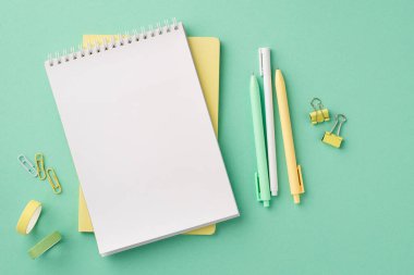 Okul konseptine geri dönelim. Kırtasiyenin en üstteki görüntüsü açık planlı kalemler bağlayıcı klipler ve izole edilmiş pastel yeşil arkaplan üzerine yapıştırıcı bant boş alan