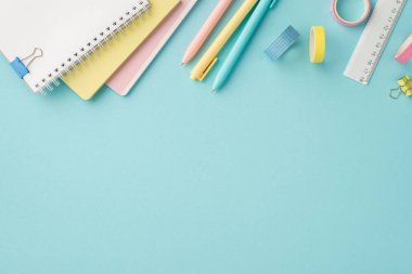 Okul konseptine geri dönelim. Okul aksesuarları yığını renkli kalemler yapışkan bant cetvelleri ve izole edilmiş pastel mavi arkaplan üzerindeki bağlayıcı kliplerin üst görünümü boş alan