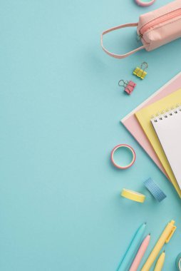 Okul konseptine geri dönelim. Renkli okul malzemelerinin dikey üst görüntüsü notlar pembe kalem kutusu yapışkan bant kalemler ve izole edilmiş pastel mavi arka plan üzerine klasör klipleri