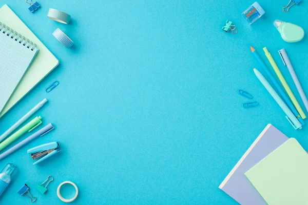 Back to school concept. Top view photo of blue stationery notepads adhesive tape binder clips pens pencil mini stapler sharpener and round correction tape on isolated blue background with copyspace