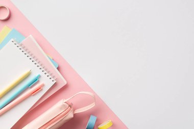 Okul konseptine geri dönelim. Okul malzemelerinin en üstteki fotoğrafı kopya defterleri renkli kalemler, kalem kılıfı ve çift renkli beyaz ve pembe arkaplan üzerine yapıştırıcı bant.