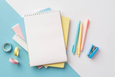 Back to school concept. Top view photo of school supplies stack of notepads pens ruler stapler and adhesive tape on bicolor blue and white background with copyspace