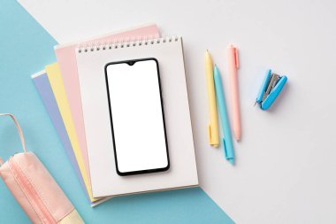 Okul malzemeleri konsepti. Akıllı telefonun üst görünüm fotoğrafı not defterleri üzerinde kalem kutusu ve bicolor mavi ve beyaz arkaplan üzerine mini zımba boş alan