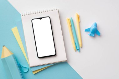 School supplies concept. Top view photo of mobile phone over notebooks plane shaped sharpener pens and pencil-case on bicolor blue and white background with copyspace
