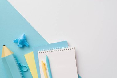 Okul konseptine geri dönelim. Sarı ve mavi okul aksesuarlarının üst görünümü notlar uçak şekilli kalemler ve çift renkli beyaz ve mavi arkaplan üzerine mavi kalem çantası