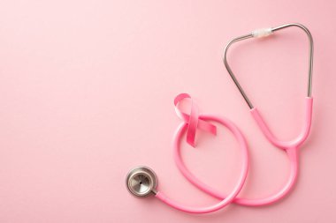 Göğüs kanseri önleme konsepti. Stetoskop üzerinden pembe kurdelenin en üstteki fotoğrafı izole edilmiş pastel pembe arka plan ve boş alan.