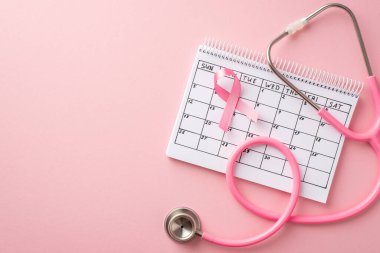 Göğüs kanseri farkındalık takviminin pembe kurdele sembolü ve izole edilmiş pastel pembe arka planlı steteskop.