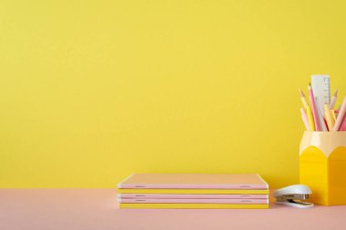 Okul konseptine geri dönelim. Okul aksesuarlarının pembe masa başı kalem tutacağı yığını ve sarı duvar zemininde fotokopi alanı olan zımba.