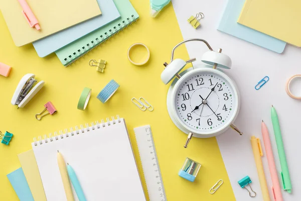 Okul aksesuarları konsepti. Alarm saatinin üst görünümü, renkli notlar, cetvel, cilt klipleri, yapıştırıcı bant ve zımba, iki renkli sarı ve beyaz arkaplan.