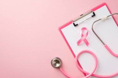 Top view photo of pink ribbon symbol of breast cancer awareness on clipboard and stethoscope on isolated pastel pink background