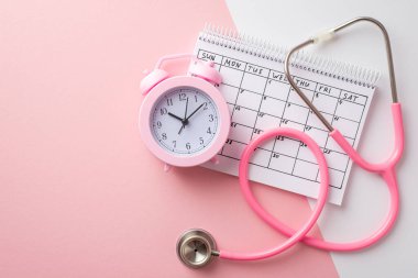 Breast cancer awareness concept. Top view photo of pink alarm clock calendar and stethoscope on bicolor pastel pink and white background