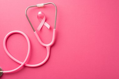 Breast cancer awareness concept. Top view photo of pink ribbon and stethoscope on isolated pink background with copyspace