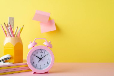 Back to school concept. Photo of school supplies pink alarm clock stack of notebooks pencils holder mini stapler and sticky note paper attached to yellow wall