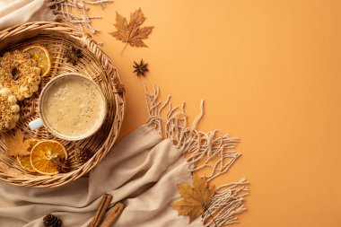 Autumn inspiration concept. Top view photo of wicker basket with cup of cocoa cookies dried orange slices anise yellow maple leaves cinnamon sticks scarf and pine cones on isolated orange background