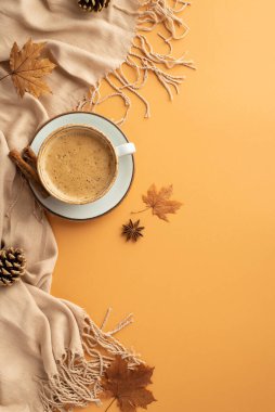 Autumn concept. Top view vertical photo of cup of hot drinking on saucer cinnamon sticks anise autumn maple leaves scarf and pine cones on isolated orange background