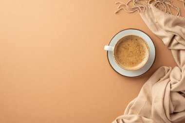 Autumn aesthetic concept. Top view photo of cup of cocoa on saucer and plaid on isolated beige background with copyspace