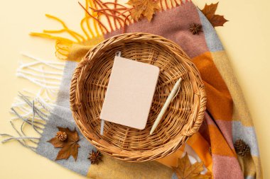 Autumn inspiration concept. Top view photo of reminder and pen in wicker basket anise yellow maple leaves pine cones and scarf on isolated pastel beige background